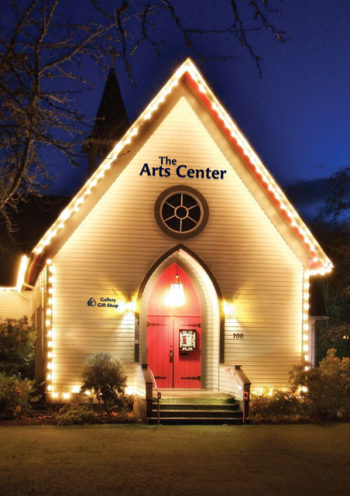 The Arts Center building shot at night with white holiday lights outlining the gothic features of the building and its prominent red door.