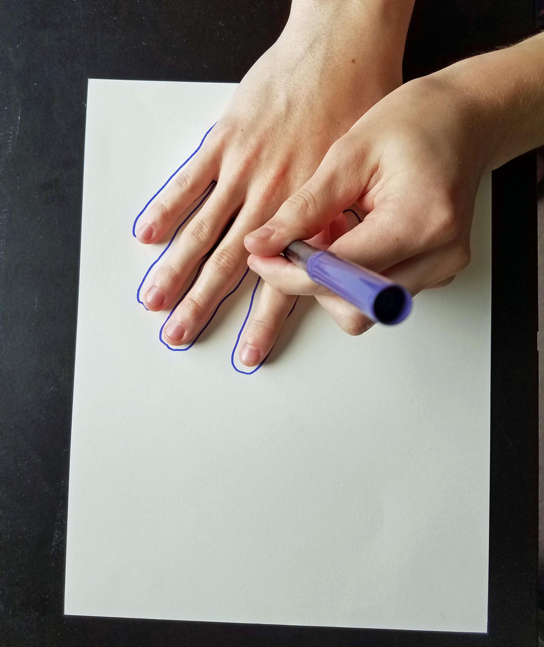 two youth hands, one tracing around handprint with purple marker