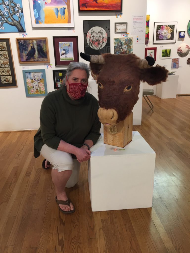Artist kneeling next to their award winning felted wool sculpture of a bull
