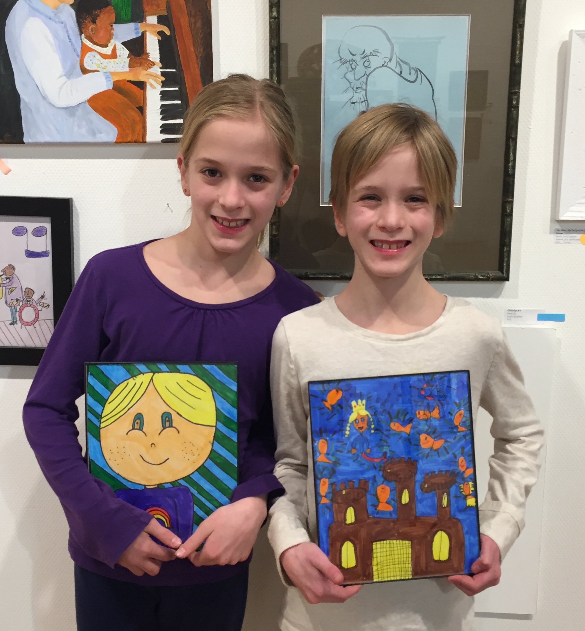 Photo of two 9 year olds holding artwork pieces in front of wall of artwork