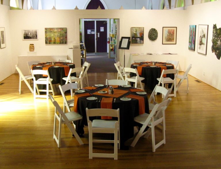 Gallery space with round tables, chairs set up for event.