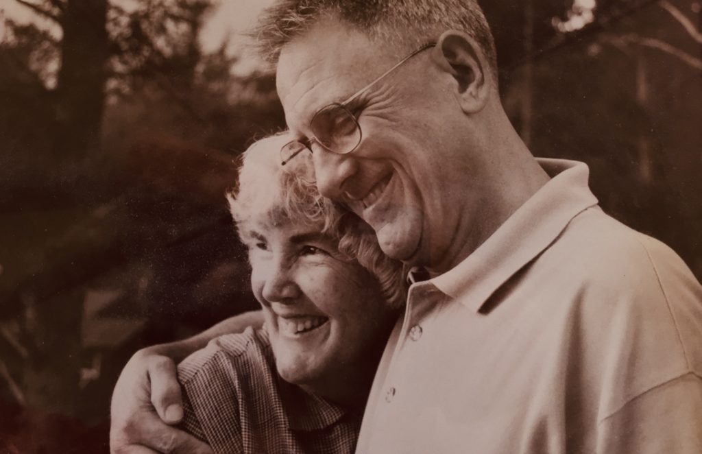 sepia toned photo showing two people middle-aged, white haired Ann Staley and Courtney Cloyd hugging each other with broad smiles 