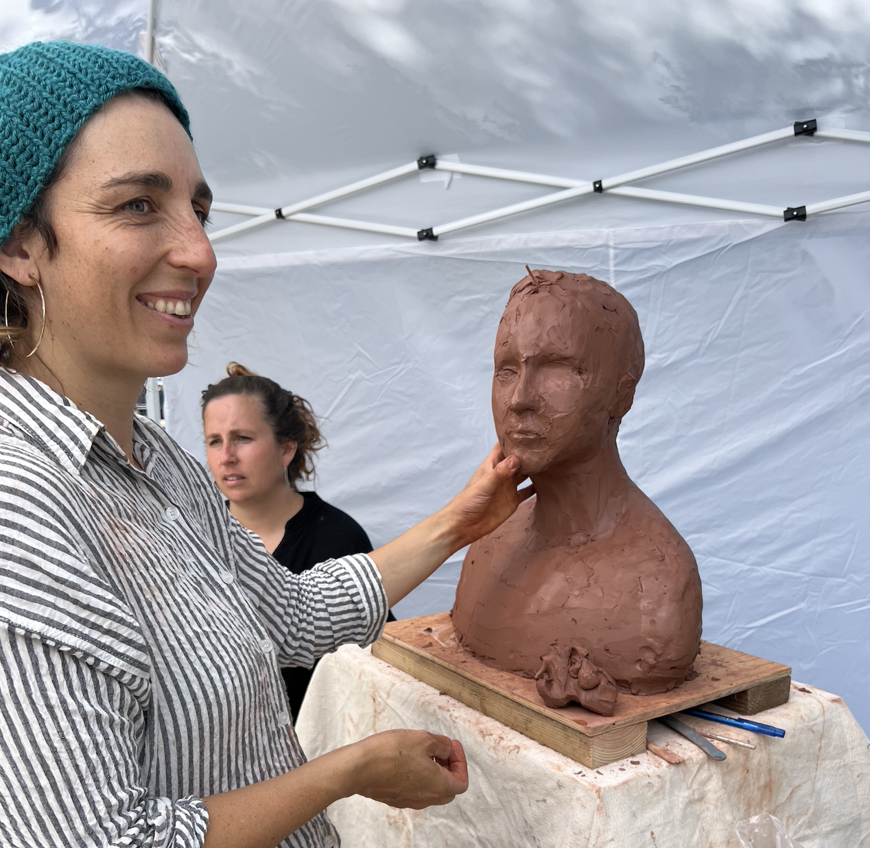 Artist Jess Felix works on a clay bust with her subject in the background. 